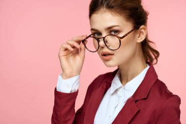 Kırmızı ceketli zarif bir kadın. Gözlüklü. Ofis müdürü, pembe arka plan.