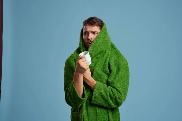 Homem congelado em um manto quente com uma xícara de bebida quente em um fundo azul vista cortada — Fotografia de Stock