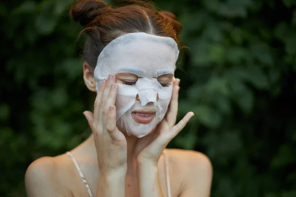 Belle femme Avec les yeux fermés, touche son visage avec ses mains masque blanc soin de la peau — Photo