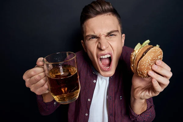 Mann mit Bierkrug und Hamburger in der Hand Spaß Lifestyle-Studio dunkel isoliert Hintergrund — Stockfoto