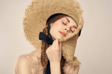 Siyah kurdeleli, saman şapkalı ve bej arka planda kırpılmış manzaralı şirin bir kız.