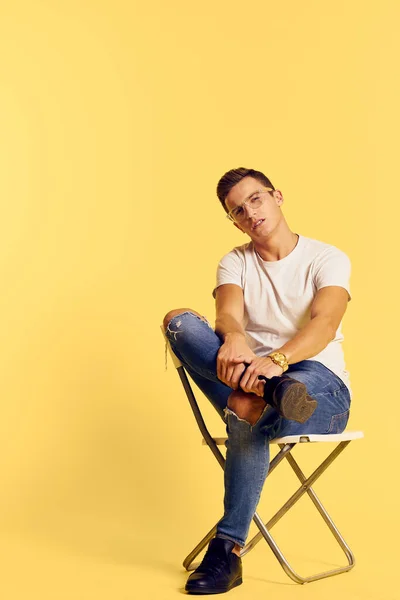 Cute man sitting on a chair white t-shirt jeans lifestyle modern style yellow background