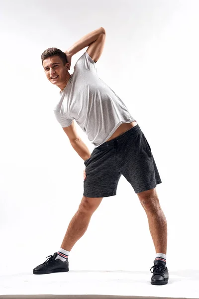 Een sportman in shorts en een full-length T-shirt doet oefeningen op een lichte achtergrond — Stockfoto