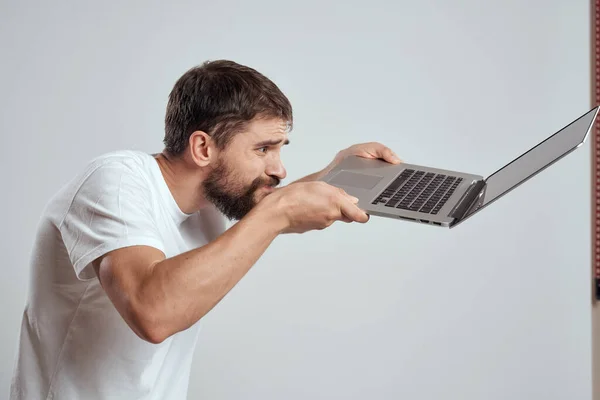 Um homem com um laptop em suas mãos em um fundo leve em uma camiseta branca emoções luz de fundo novas tecnologias — Fotografia de Stock