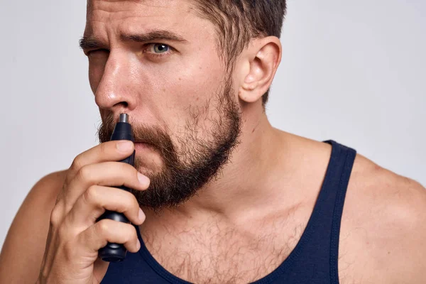 Un uomo con una macchina per rimuovere i capelli da un naso in una t-shirt nera leggera cura del corpo di sfondo — Foto Stock