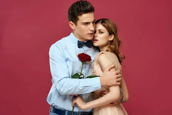 Влюблённые мужчина и женщина с красным цветком на розовом фоне обнимают друг друга — стоковое фото