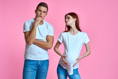 Hamile anne ve mutlu baba pembe arka planda genç aile bebek bekliyor.