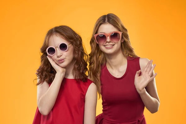 Happy woman and little girl in red dress are having fun on a yellow background fashion emotions sisters fun Copy Space. — Stock Photo, Image