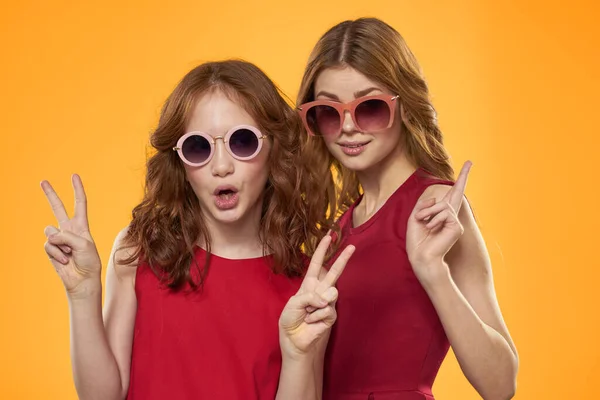 Mujer feliz y niña en vestido rojo se divierten en un fondo amarillo moda emociones hermanas diversión Copiar espacio. — Foto de Stock