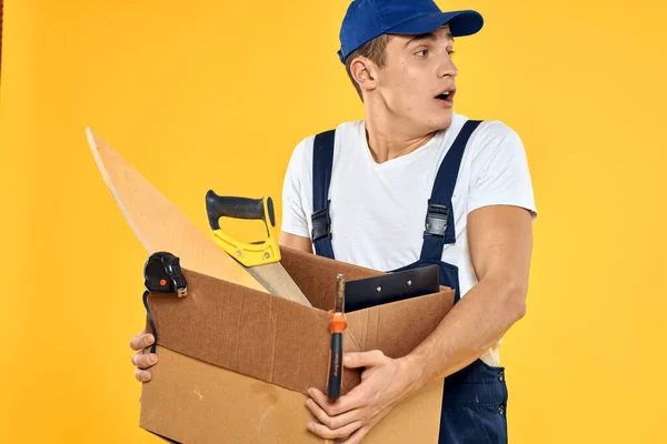 Pracovník s krabicí v ruce nářadí nakladač žluté pozadí — Stock fotografie