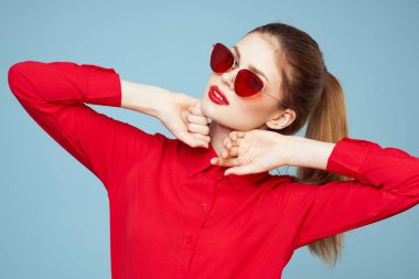 Koyu renk gözlüklü, kırmızı dudaklı, cazibeli stüdyo mavi arka planlı bir kadın.