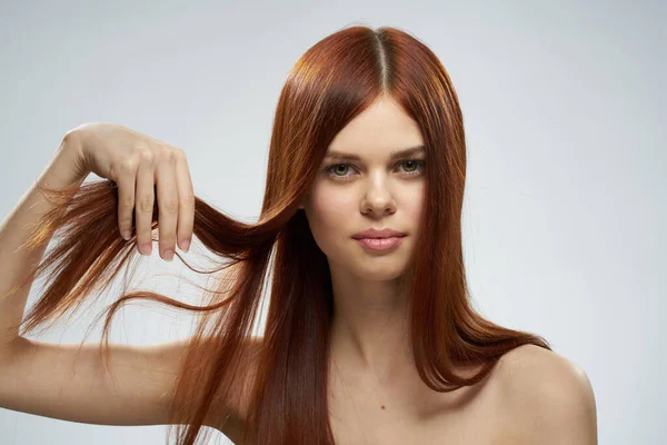 Όμορφη κοκκινομάλλα γυναίκα κρατώντας τα μαλλιά της με τα χέρια περιποίηση γυμνή ώμους φως φόντο — Φωτογραφία Αρχείου