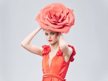 Kırmızı elbiseli kadın başının üstünde süslü bir çiçek tutuyor.