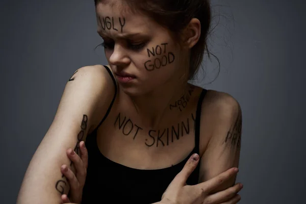 Beleidigte Frau mit wütenden Schriftzügen auf ihrem Körper berührt sich mit den Händen auf grauem Grund — Stockfoto