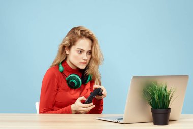 Dizüstü bilgisayar kulaklığının önündeki masada oturan bir kadın çevrimiçi yaşam tarzı mavi arka planda oynuyor.