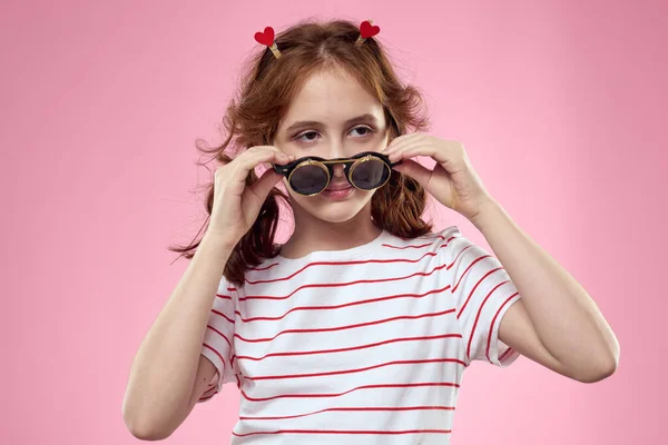 Χαρούμενο κορίτσι με κοτσιδάκια γυαλιά ηλίου ριγέ t-shirt lifestyle ροζ φόντο — Φωτογραφία Αρχείου