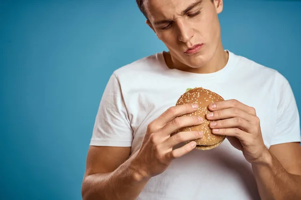 Hombre con hamburguesa y camiseta blanca fondo azul emociones gestos con las manos Copiar espacio — Foto de Stock