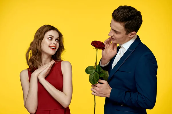 Milenci muži žena s červenou růží v rukou romantika dovolená žluté pozadí rodina přátelé. — Stock fotografie