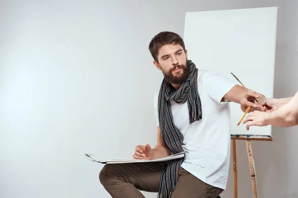 Maschio artista seduto sulla sedia disegno pennello cavalletto hobby creativo luce sfondo — Foto Stock
