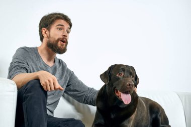 Beyaz bir kanepede siyah köpeği olan bir adam. Arka planda, yakın planda kesilen evcil hayvan insan arkadaş duyguları. Eğlenceli.