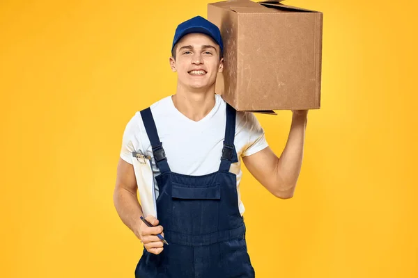 Working man in uniform with box hand delivery loading service yellow background — Stock Photo, Image