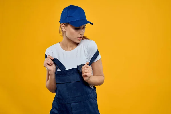 Kvinna i arbetande uniform blå mössa leverera kurir service gul bakgrund — Stockfoto