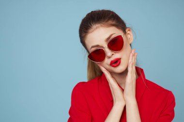 Mavi arka plandaki kırmızı gömlekli kadın yüz ve güneş gözlüklü kırmızı dudak makyajı modeli ile el ele tutuşuyor.