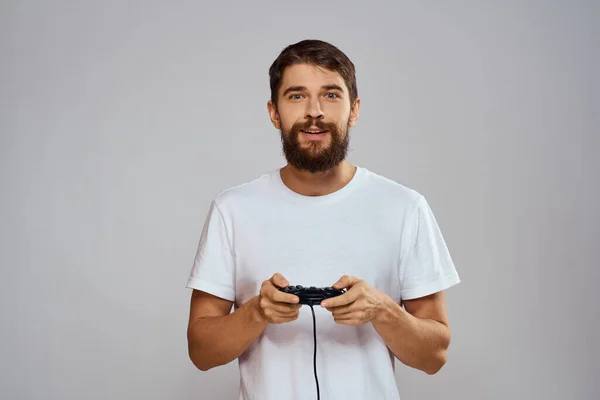 Een man met een gamepad in zijn handen spelen spelletjes vrije tijd lifestyle technologie wit t-shirt lichte achtergrond — Stockfoto