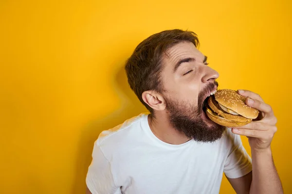 Homem com hambúrguer nas mãos de fast food dieta comida branca t-shirt close-up fundo amarelo — Fotografia de Stock