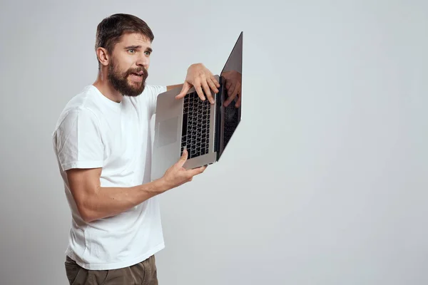 Um homem com um laptop em suas mãos em um fundo leve em uma camiseta branca emoções luz de fundo novas tecnologias — Fotografia de Stock