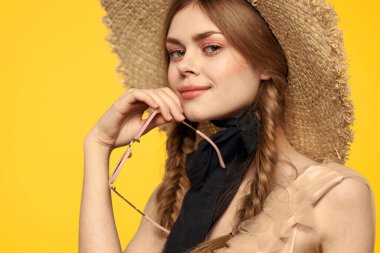 Şapkalı romantik bir kadın sarı arka planda eğleniyor ve güneş gözlüğü siyah kurdele modeli portresi takıyor.