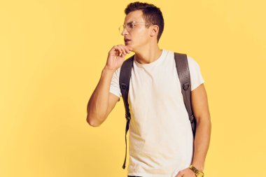 Beyaz tişörtlü yakışıklı adam sırt çantalı şık kıyafetler modern tarz gençlik sarısı arka plan