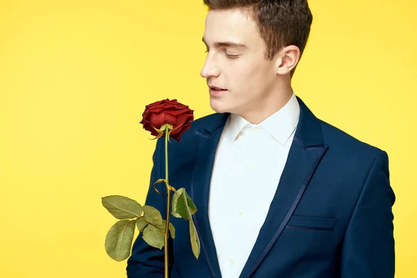 Junger Mann im klassischen Anzug mit roter Rose in der Hand auf gelbem Hintergrund — Stockfoto