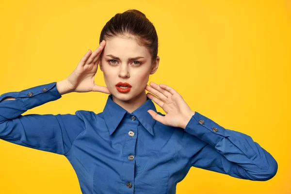 Retrato de uma mulher em uma camisa azul com maquiagem brilhante lábios vermelhos fundo amarelo vista recortada — Fotografia de Stock