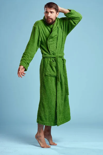 Um homem em um manto verde em pleno crescimento em um fundo azul descalço — Fotografia de Stock