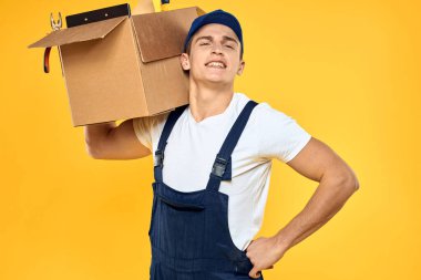Kutu teslimat servisi sarı arka planda üniformalı bir işçi.
