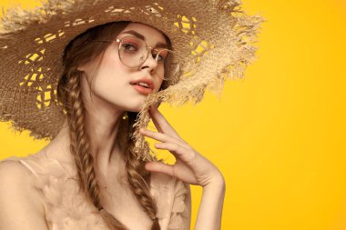 Saçları örgülü ve sarı arka planda şapkası olan güzel bir kadının portresi.