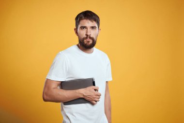 Beyaz tişörtlü, sarı arka planda tabletli bir adam. Yeni teknoloji işadamı ekranda dokunuyor.