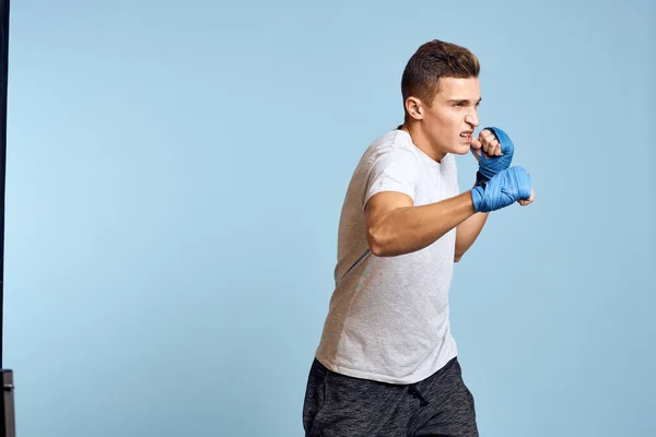 Uomo sportivo in guanti da boxe blu e t-shirt su sfondo blu praticando pugni vista ritagliata — Foto Stock