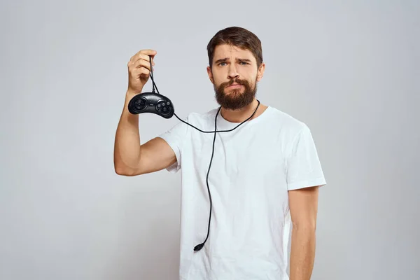 Ένας άνθρωπος με ένα gamepad στα χέρια του παίζοντας παιχνίδια αναψυχής lifestyle τεχνολογία λευκό t-shirt φως φόντο — Φωτογραφία Αρχείου