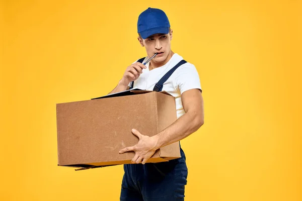 Pracující muž v uniformě s krabicí ruční dodání služby žluté pozadí — Stock fotografie