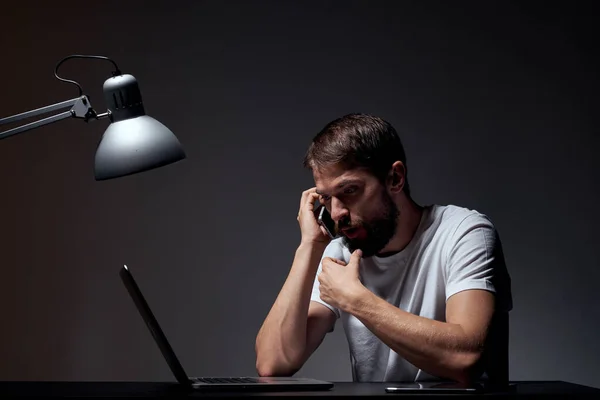 man with laptop sitting at table dark background workplace office emotions lamp gesturing with hands model cropped view