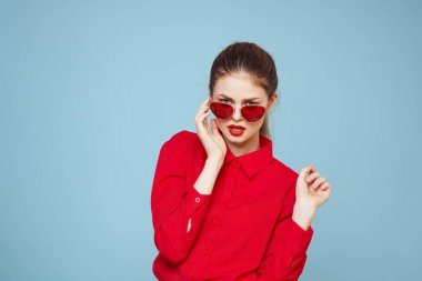 Koyu renk gözlüklü, kırmızı dudaklı, cazibeli stüdyo mavi arka planlı bir kadın.