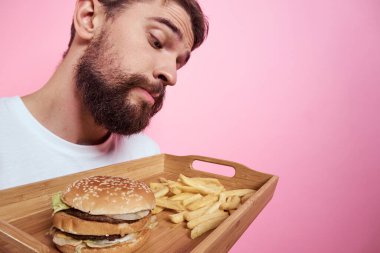 Elinde yemek tepsisi olan bir adam hamburger kızartması ve fast food kalorisi pembe arka plan portresi.