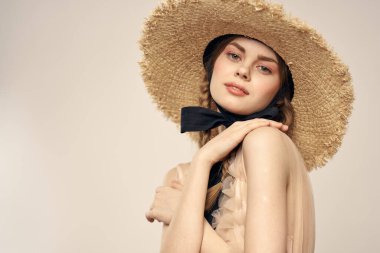Hasır şapkalı, siyah kurdeleli ve arka planda açık bir elbise giyen hoş bir kız. Romantik bir model.