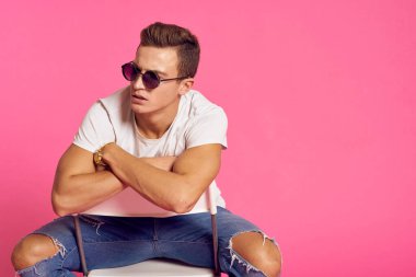 Beyaz tişörtlü ve kot pantolonlu bir adam, modern tarz pembe izole edilmiş arka planda oturuyor.