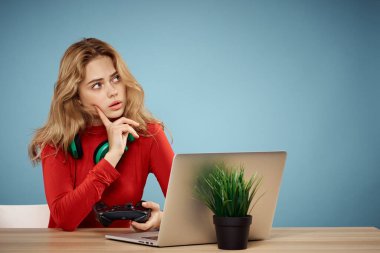 Dizüstü bilgisayar kulaklığının önündeki masada oturan bir kadın çevrimiçi yaşam tarzı mavi arka planda oynuyor.