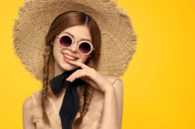Şapkalı romantik bir kadın sarı arka planda eğleniyor ve güneş gözlüğü siyah kurdele modeli portresi takıyor.