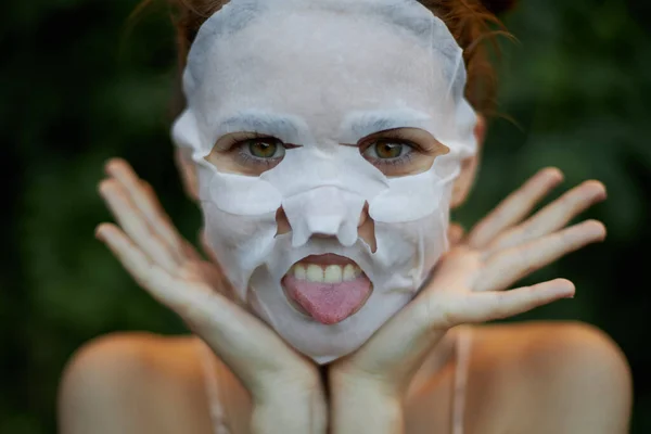 Hermosa máscara facial mujer muestra la lengua y sostiene las manos cerca de la dermatología facial —  Fotos de Stock