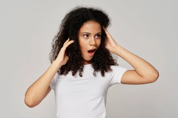 Mulher surpresa com cabelo encaracolado e camiseta branca em fundo isolado — Fotografia de Stock